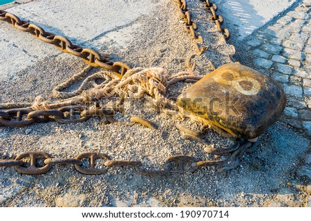 Old and rust mooring bollard with ropes and chains