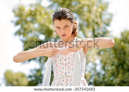 A pretty young woman is playing with a scarf in the park, the strong summer sun lights her in back light.