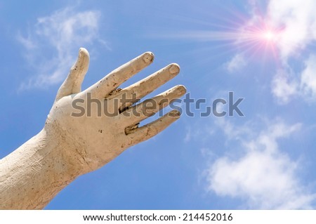 A statue hand showing the sun in the cloudy blue sky, as idea of freedom