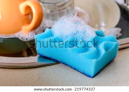 Cleaning the dirty dishes with a blue sponge with detergent in a sink