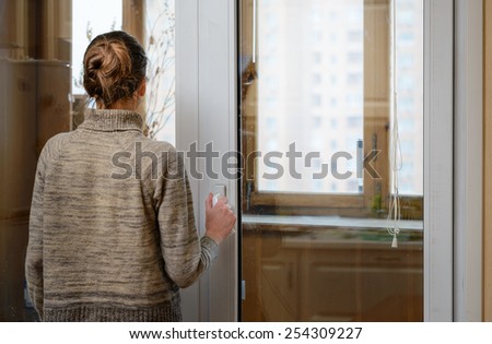 A woman is looking the city through the window during a sad winter day