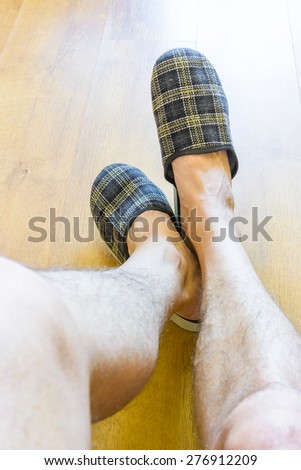 A man is relaxing while wearing warm slippers and showing hairy legs