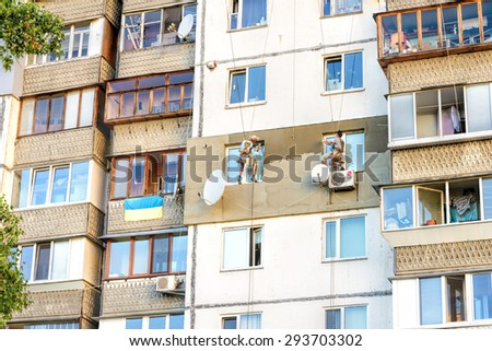 Kiev, Ukraine - June 30, 2015:  Facade plasterers build the  external thermal insulation of an apartment sitting on their swing, suspended in midair