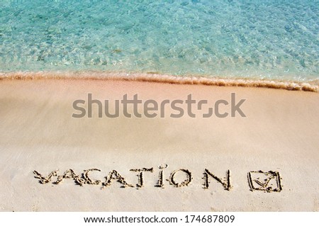 Vacation and checked mark written on sand on a beautiful beach, blue waves in background