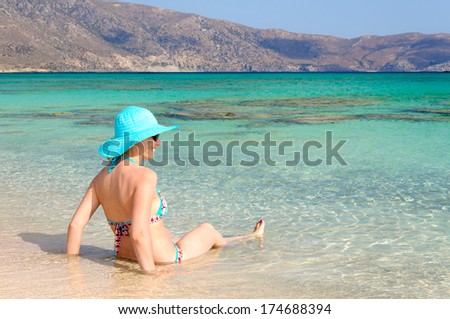 Beautiful young woman in swimsuit with sunhat, relaxing on the sunny beach. Chill out concept