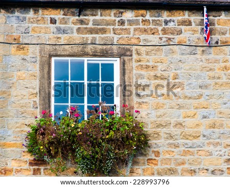 Architecture detail of traditional English cottage, with pots of flowers at the window and British flag on the wall