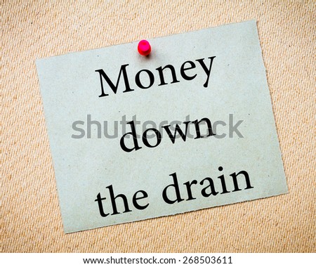 MONEY DOWN THE DRAIN Message. Recycled paper note pinned on cork board. Concept Image