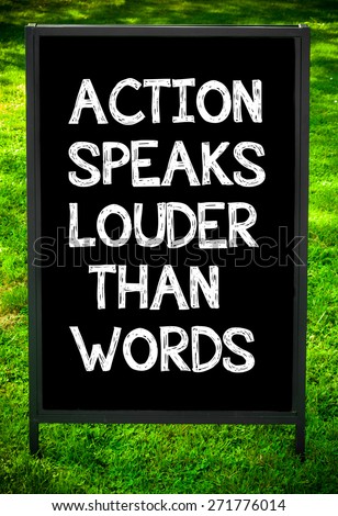 ACTION SPEAKS LOUDER THAN WORDS  message on sidewalk blackboard sign against green grass background. Copy Space available. Concept image