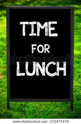 TIME FOR LUNCH  message on sidewalk blackboard sign against green grass background. Copy Space available. Concept image