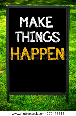 MAKE THINGS HAPPEN  message on sidewalk blackboard sign against green grass background. Copy Space available. Concept image