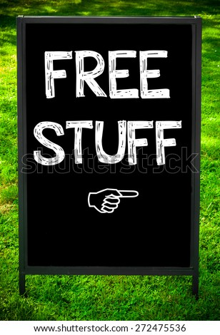 FREE STUFF message on sidewalk blackboard sign against green grass background. Copy Space available. Concept image