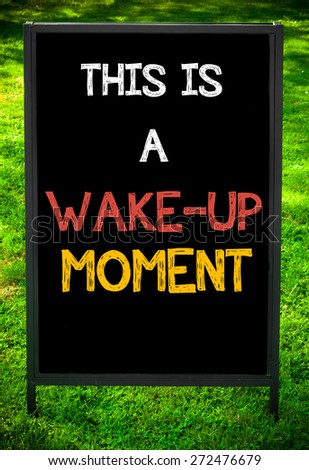 THIS IS A WAKE-UP MOMENT message on sidewalk blackboard sign against green grass background. Copy Space available. Concept image