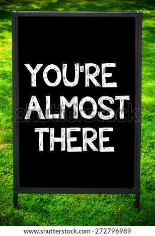 YOU\'RE ALMOST THERE  message on sidewalk blackboard sign against green grass background. Copy Space available. Concept image