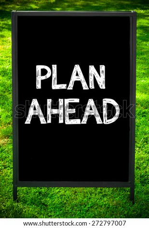 PLAN AHEAD  message on sidewalk blackboard sign against green grass background. Copy Space available. Concept image