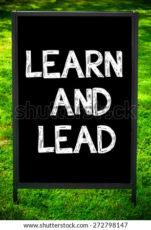 LEARN AND LEAD  message on sidewalk blackboard sign against green grass background. Copy Space available. Concept image