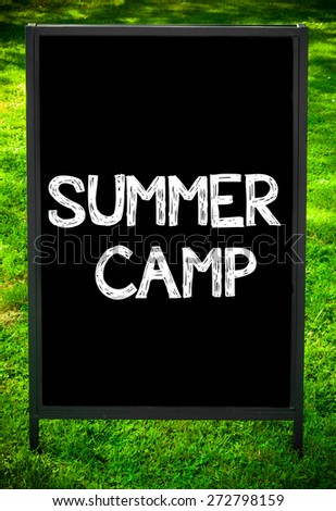 SUMMER CAMP  message on sidewalk blackboard sign against green grass background. Copy Space available. Concept image
