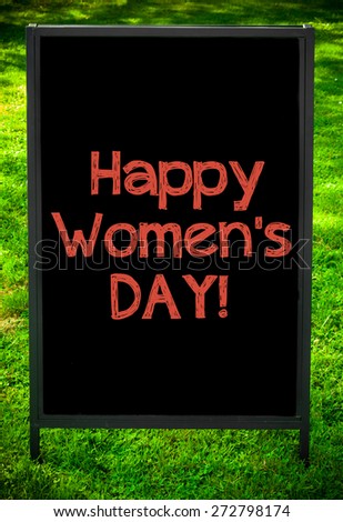 HAPPY WOMEN\'S DAY  message on sidewalk blackboard sign against green grass background. Copy Space available. Concept image
