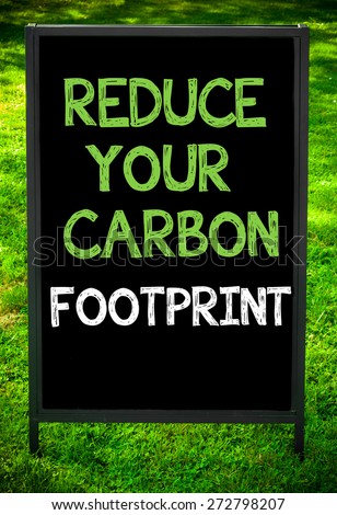 REDUCE YOUR CARBON FOOTPRINT  message on sidewalk blackboard sign against green grass background. Copy Space available. Concept image
