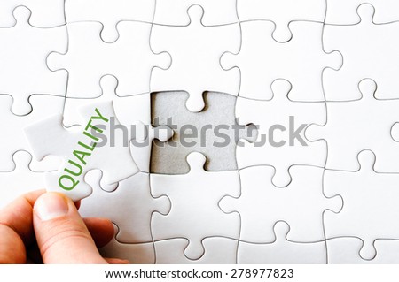 Hand with missing jigsaw puzzle piece. Word QUALITY. Business concept image for completing the final puzzle piece.
