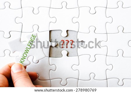 Hand with missing jigsaw puzzle piece. Word KNOWLEDGE, covering  QUESTION MARKS.. Business concept image for completing the final puzzle piece.