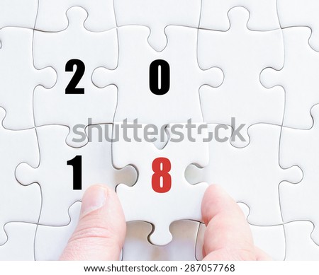 Hand of a business man completing the puzzle with the last missing piece. Concept image of puzzle board with year 2018