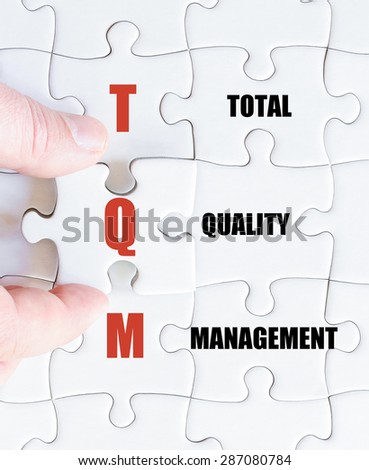 Hand of a business man completing the puzzle with the last missing piece.Concept image of Business Acronym TQM as Total Quality Management