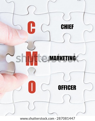 Hand of a business man completing the puzzle with the last missing piece.Concept image of Business Acronym CMO as Chief Marketing Officer