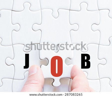 Hand of a business man completing the puzzle with the last missing piece.Concept image of puzzle board with motivational word JOB