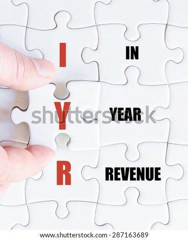 Hand of a business man completing the puzzle with the last missing piece.Concept image of Business Acronym IYR as In Year Revenue