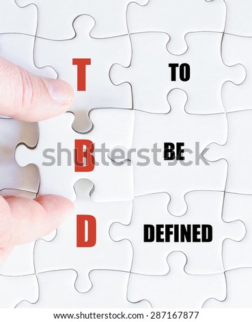 Hand of a business man completing the puzzle with the last missing piece.Concept image of Business Acronym TBD as To Be Defined
