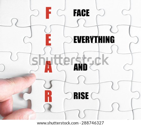 Hand of a business man completing the puzzle with the last missing piece.Concept image of Business Acronym FEAR as Face Everything And Rise