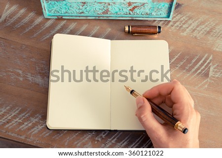 Retro effect and toned image of a woman hand writing a note with a fountain pen on a notebook. Copy space available