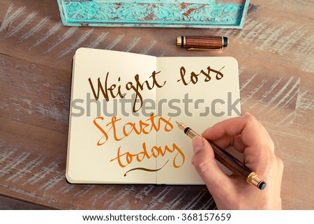Retro effect and toned image of a woman hand writing a note with a fountain pen on a notebook. Handwritten text WEIGHT LOSS STARTS TODAY, motivation concept