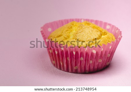 Tasty fresh golden muffin or cupcake in a pink fluted casing for a special occasion on a pink studio background with copy space