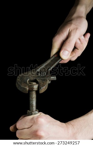 Worker\'s hands screwing the nut with the rusty adjustable wrench on black background.