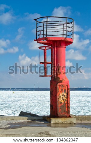 Abandoned navigation light mast on a pier, frozen sea behind it