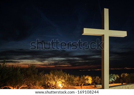 Cross on the hill, between olive trees, sunset in background.