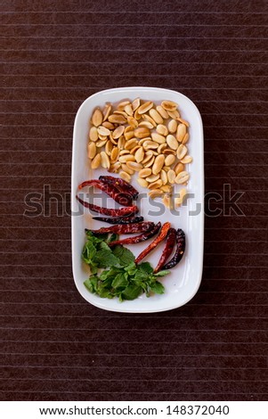 spices, peanut and Basil on white dish on dark wood table