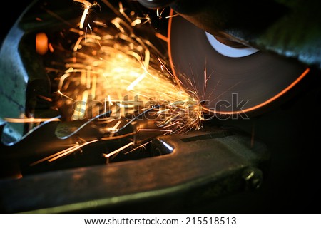 Flying sparks from a spinning grinder sharpening the teeth of an industrial saw. The edge of the grinder stone is glowing from frictional heat.