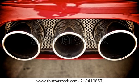 Triple exhaust pipes of car with red body finish. Exhausts and grille have a polished chrome finish and are viewed from behind and above.