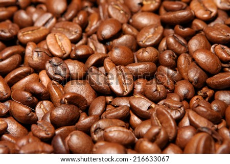 Close view of randomly stacked coffee beans fills the frame. Roasted beans in shades of brown color forming a plane. Visible details, indoor lighting.