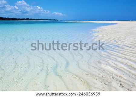 Wide angle view of rippled white sand reef party covered with clear turquoise waters of the Indian Ocean. Blue sky with clouds. Near Diani Beach, Kenya.