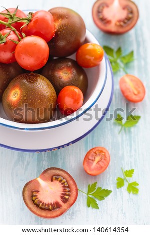 Three varieties of whole and halved tomato on a plate including grape tomatoes, cherry tomatoes and a purple-red variety
