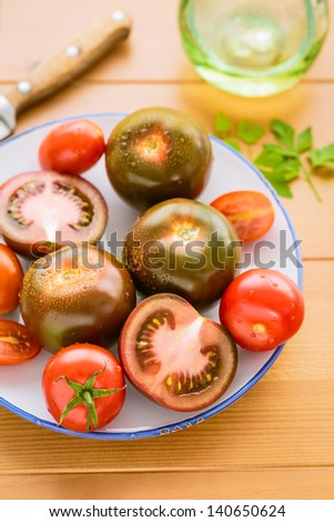 Three varieties of whole and halved tomato on a plate including grape tomatoes, cherry tomatoes and a purple-red variety