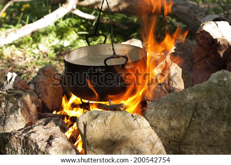 Pot water on the fire, tourists kettle on hot campfire. Camping photo.