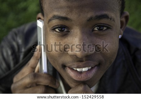 african boy on cell phone outside sitting on  grass