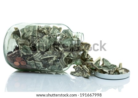 Glass jar full of money tipped over on its side spilling money with lid