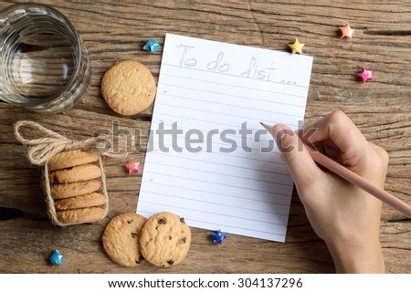 woman hand write to do list on wooden table with chocolate chip cookie