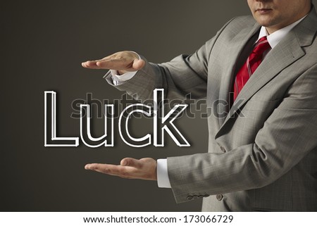Young businessman in a black suit and tie holding a word Luck on a gray background. Concept of problem and solution. Slide presentation.