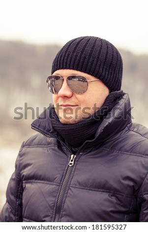 male portrait with sun glasses wearing black hat and scarf in autumn, winter, spring season outdoor